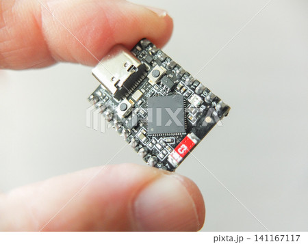 Hand holding a small black microchip microcontroller development board with type-c Hand holding a small black microchip microcontroller development board with type-c 141167117