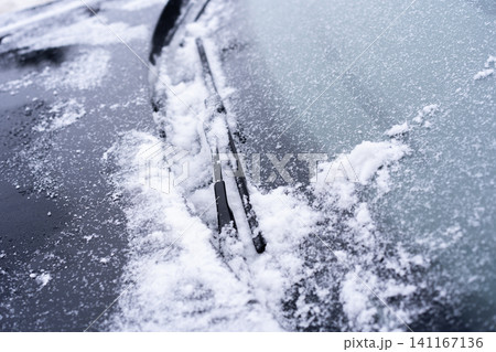Close-up of a car windshield covered with snow and ice, with wiper blades resting against the glass. Close-up of a car windshield covered with snow and ice, with wiper blades resting against the glass. 141167136