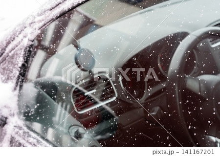 Close-up of a car window covered with delicate snowflakes. The crystalline patterns stand out against the reflective surface, where faint outlines of the surroundings appear blurred. Close-up of a car window covered with delicate snowflakes. The crystalline patterns stand out against the reflective surface, where faint outlines of the surroundings appear blurred. 141167201