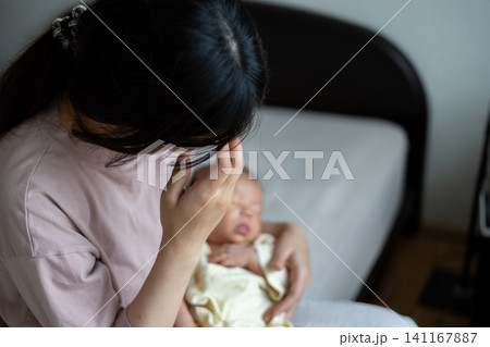 赤ちゃんを抱いた産後疲れの出た新米ママさん 赤ちゃんを抱いた産後疲れの出た新米ママさん 141167887