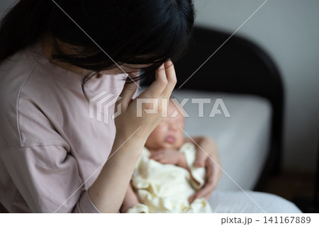 赤ちゃんを抱いた産後疲れの出た新米ママさん 赤ちゃんを抱いた産後疲れの出た新米ママさん 141167889