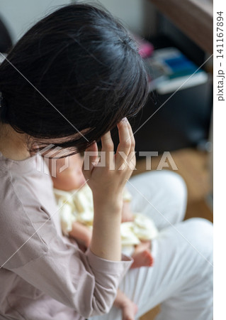 赤ちゃんを抱いた産後疲れの出た新米ママさん 赤ちゃんを抱いた産後疲れの出た新米ママさん 141167894