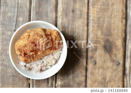 ご飯の上に乗せたカリッとジューシーな鶏もも肉の大きな唐揚げ 141168840