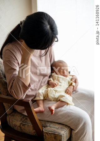 赤ちゃんを抱いた産後疲れの出た新米ママさん 赤ちゃんを抱いた産後疲れの出た新米ママさん 141168926