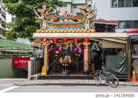 A small, ornate traditional Taoist street shrine with colorful roof decorations and paper lanterns in Taipei, Taiwan. A small, ornate traditional Taoist street shrine with colorful roof decorations and paper lanterns in Taipei, Taiwan. 141169980