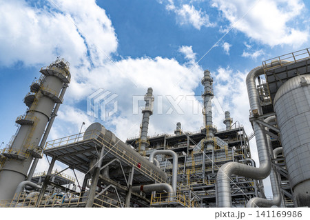 Low-angle view of massive distillation towers and complex pipeline systems at a modern petrochemical refinery plant under a blue sky 141169986