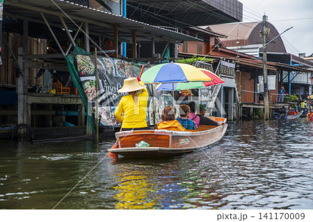 Tourists on a traditional wooden boat exploring a famous floating market in Thailand. Tourists on a traditional wooden boat exploring a famous floating market in Thailand. 141170009