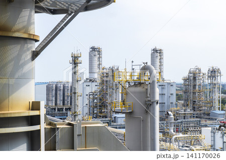 Industrial background of a large-scale chemical factory and oil refinery with complex pipelines, distillation towers, and storage tanks under a clear sky. Industrial background of a large-scale chemical factory and oil refinery with complex pipelines, distillation towers, and storage tanks under a clear sky. 141170026