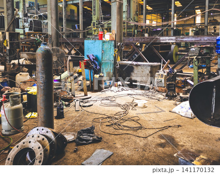 Interior view of a cluttered heavy industrial workshop with gas cylinders, flanges, and welding equipment 141170132