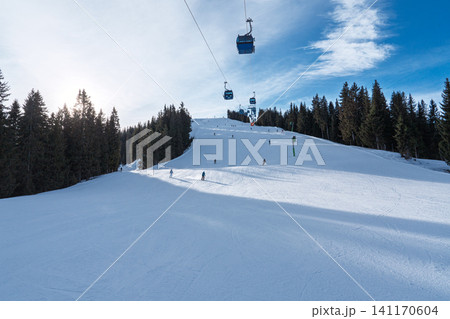 Skiers on a groomed slope with cable cars in the winter landscape of Saalbach in Austria Skiers on a groomed slope with cable cars in the winter landscape of Saalbach in Austria 141170604