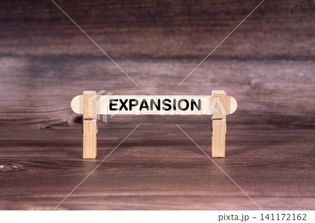 Expansion symbol. Clothespins gripping a wooden stick against a beautiful Brown Wooden Background . Business and Expansion concept with copy space Expansion symbol. Clothespins gripping a wooden stick against a beautiful Brown Wooden Background . Business and Expansion concept with copy space 141172162