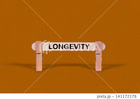 Longevity symbol. Wooden stick tightened by Clothespins, beautiful Orange color Backdrop. Business and Longevity concept with copy space Longevity symbol. Wooden stick tightened by Clothespins, beautiful Orange color Backdrop. Business and Longevity concept with copy space 141172178