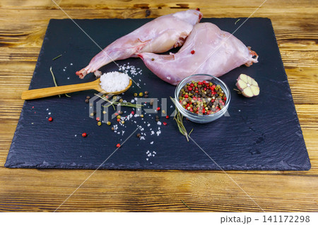 Raw rabbit legs with spices on a black slate cutting board on wooden table Raw rabbit legs with spices on a black slate cutting board on wooden table 141172298