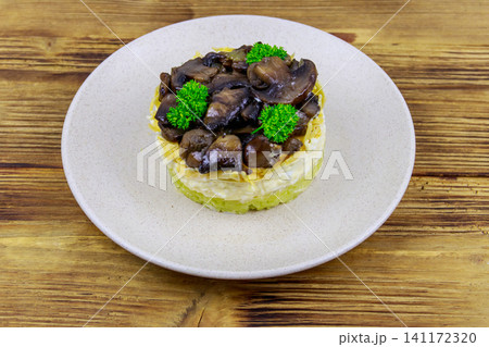 Tasty layered salad with roasted mushrooms, potato, eggs, cheese and mayonnaise on wooden table 141172320