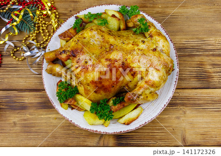 Baked whole chicken with potato and Christmas decorations on a wooden table. Top view Baked whole chicken with potato and Christmas decorations on a wooden table. Top view 141172326