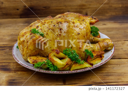 Baked whole chicken with potato on a wooden table Baked whole chicken with potato on a wooden table 141172327