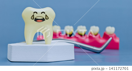 Sad crying tooth model on white podium with dental tool and jaw model with caries in blurred background. Pediatric dentistry concept. 141172701