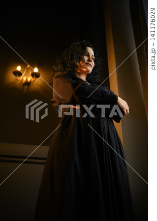 Woman stands in a dimly lit room with candles and natural light coming through a window Woman stands in a dimly lit room with candles and natural light coming through a window 141176029