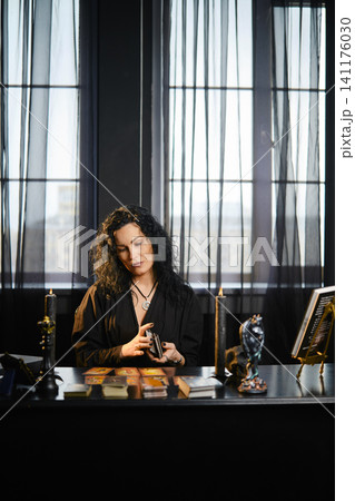 Woman reads tarot cards in a dark room with large windows and curtains Woman reads tarot cards in a dark room with large windows and curtains 141176030