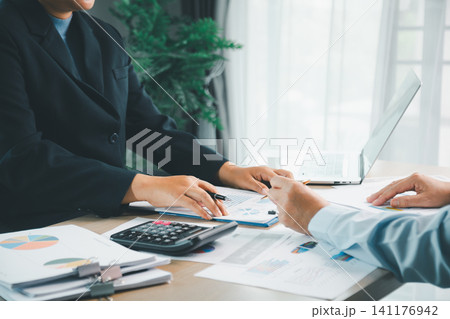 Business professionals discussing accounting documents with calculator, laptop and financial charts on desk, representing budget review, audit, tax and investment planning. Business professionals discussing accounting documents with calculator, laptop and financial charts on desk, representing budget review, audit, tax and investment planning. 141176942
