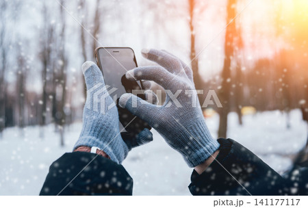 Man using smartphone in winter with gloves for touch screens Man using smartphone in winter with gloves for touch screens 141177117