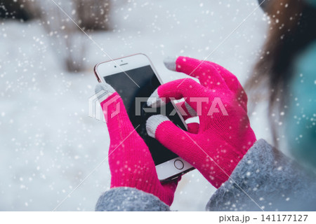 Woman using smartphone in winter with gloves for touch screens Woman using smartphone in winter with gloves for touch screens 141177127