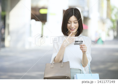 屋外でクレジットカードを手にショッピングを楽しむ30代女性 キャッシュレス決済 141177149
