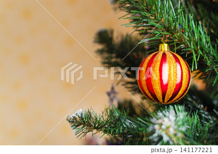 Red striped Christmas bauble hanging on a fir tree branch with copy space. Traditional holiday decoration and festive celebration concept for greeting cards and seasonal marketing. 141177221