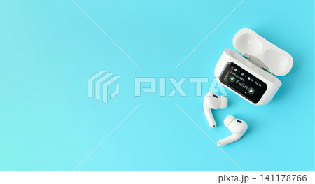 White wireless earbuds with a smart charging case on a blue background. Modern audio technology concept for music, communication and mobile lifestyle White wireless earbuds with a smart charging case on a blue background. Modern audio technology concept for music, communication and mobile lifestyle 141178766