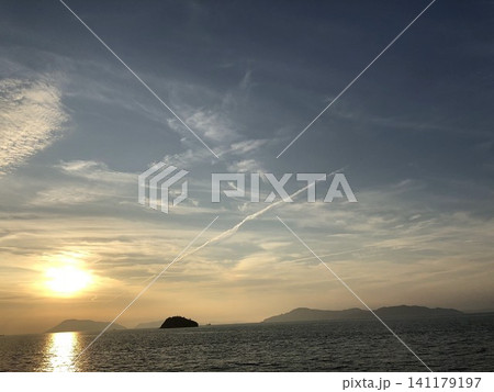 穏やかな海に沈む夕日と島影 飛行機雲のある空 穏やかな海に沈む夕日と島影 飛行機雲のある空 141179197
