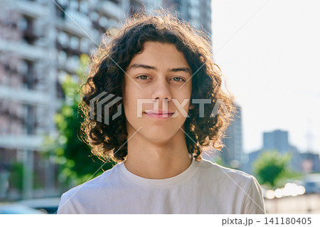 Happy curly haired teenage boy smiling outdoors on modern city street background Happy curly haired teenage boy smiling outdoors on modern city street background 141180405
