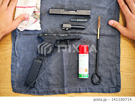 Hands, cleaning and man with gun on cloth for safety, self defense and handgun assembly. Process, equipment and person with firearm maintenance, magazine and metal parts to assemble weapon on table 141180714