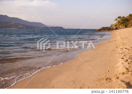 Travel, beach and sand by ocean for vacation, holiday or adventure for paradise landscape. Blue sky, nature and sun by waves or sea water on tropical island for outdoor weekend trip in summer. 141180776