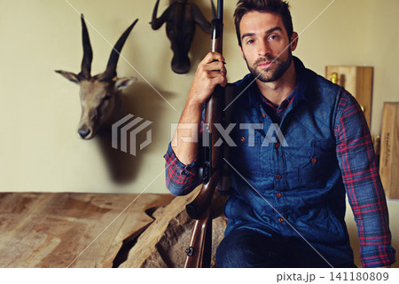 Portrait, hunter and man with trophies, gun and confidence with business and resort with achievement. Face, person and game hunter with weapon and animal heads with firearm and equipment with pride 141180809