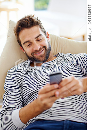 Man, happy and cellphone on couch in living room for for communication, social media and or texting. Smartphone, smile and male person for internet browsing, notification or online chat on weekend Man, happy and cellphone on couch in living room for for communication, social media and or texting. Smartphone, smile and male person for internet browsing, notification or online chat on weekend 141180947