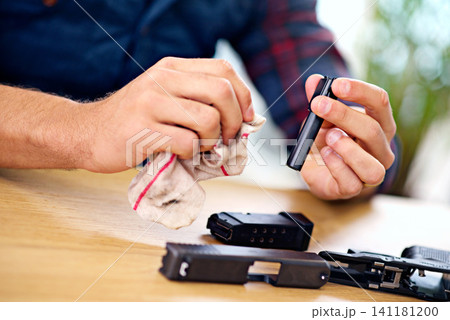 Hands, cleaning and man with gun at table for safety, self defense and handgun assembly. Process, equipment and person with firearm maintenance with cloth, magazine and wiping dust, dirt and oil Hands, cleaning and man with gun at table for safety, self defense and handgun assembly. Process, equipment and person with firearm maintenance with cloth, magazine and wiping dust, dirt and oil 141181200