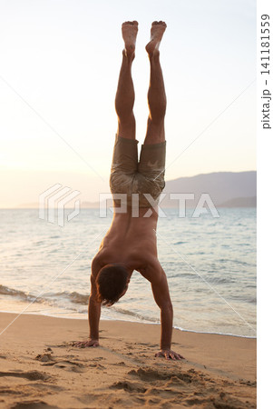 Man, beach and handstand for holiday travel on tropical island for ocean adventure, sunshine or weekend. Male person, sand and seaside fun in evening at tourism coast for break, outdoor or explore 141181559
