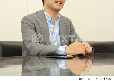 テーブルに座って話すスーツの若い男性の口元と上半身 141181600