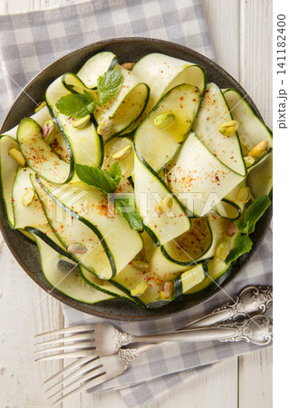 Delicious zucchini carpaccio topped with pistachios, chili pepper and mint close-up in a plate. Vertical top view Delicious zucchini carpaccio topped with pistachios, chili pepper and mint close-up in a plate. Vertical top view 141182400