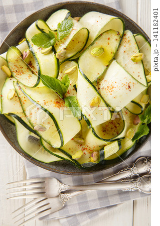 Raw zucchini ribbon carpaccio with pistachios, chili pepper and mint close-up in a plate on the table. Vertical top view 141182401