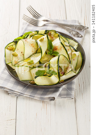 Delicious zucchini carpaccio topped with pistachios, chili pepper and mint close-up in a plate. Vertical Delicious zucchini carpaccio topped with pistachios, chili pepper and mint close-up in a plate. Vertical 141182405