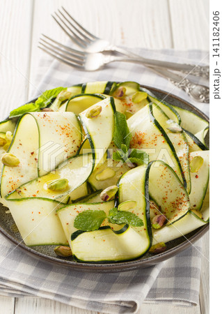 Zucchini carpaccio with pistachios, chili pepper and mint close-up in a plate. Vertical 141182406