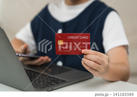 Person holding red credit card with visible chip near open laptop keyboard and smartphone in hand, online shopping and digital payment concept with casual clothing indoors Person holding red credit card with visible chip near open laptop keyboard and smartphone in hand, online shopping and digital payment concept with casual clothing indoors 141183389