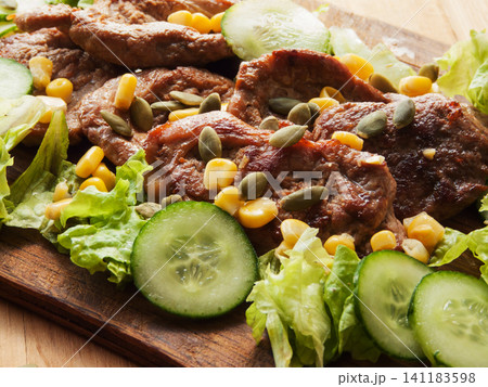 Juicy fried pork tenderloin steaks with sweet corn, green lettuce cucumbers salad and pumpkin seeds Juicy fried pork tenderloin steaks with sweet corn, green lettuce cucumbers salad and pumpkin seeds 141183598