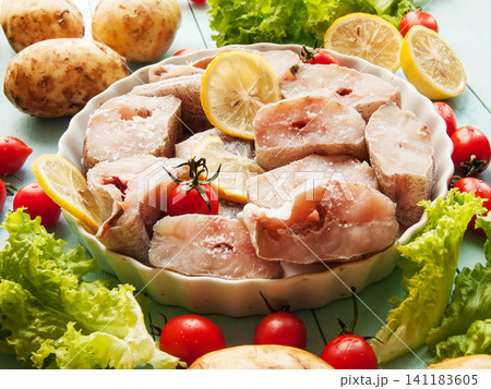 Fresh pollock seafood steaks with lettuce and cherry tomatoes seasoned with salt and lemon in pan. 141183605