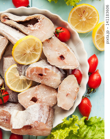 Fresh pollock seafood steaks with lettuce and cherry tomatoes seasoned with salt and lemon in pan. 141183606