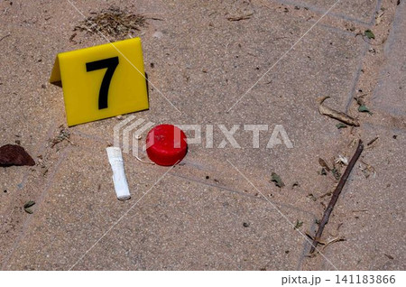 One yellow crime scene marker on the paving slab near a bottle cap and a cigarette butt 141183866