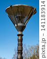 Vintage street lantern on a decorative metal pillar post against a clear blue sky in a public park 141183914