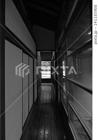 趣深い古民家の板張りの廊下 障子戸とガラス窓に挟まれた長い通路の奥から差し込む光が作り出す美しい陰影 趣深い古民家の板張りの廊下 障子戸とガラス窓に挟まれた長い通路の奥から差し込む光が作り出す美しい陰影 141185908