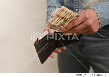 person holding wallet full of cash, showing various bills in open wallet. person holding wallet full of cash, showing various bills in open wallet. 141186694
